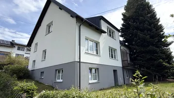 Modernisiertes Einfamilienhaus mit weißer Fassade und dunklem Dach in ländlicher Umgebung.