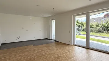 Heller, offener Wohnbereich mit Parkettboden und vorbereiteter Küchenzeile, mit Zugang zur Terrasse.