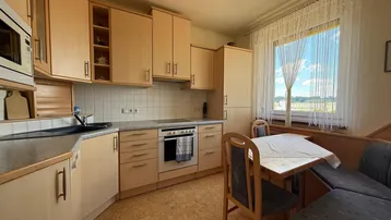 Helle Küche mit Holzschränken, integriertem Essbereich und Blick ins Grüne.