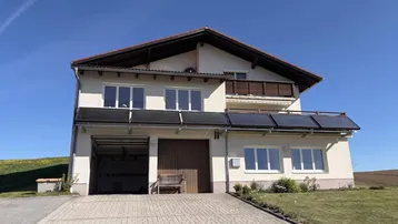 Modernes Einfamilienhaus mit gepflasterter Auffahrt, Garage und Solarpaneelen auf dem Dach.