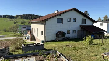 Rückansicht des Hauses mit Gartenbereich, Hochbeeten und Blick auf die grüne Landschaft.