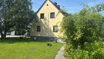 Gelbes Einfamilienhaus mit Satteldach und grünem Garten unter blauem Himmel.