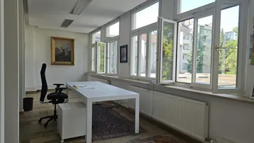 Helles Büro mit großzügigen Fenstern, Blick ins Grüne und einem modernen Schreibtisch.