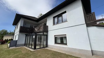 Außenansicht des Hauses mit Wintergarten, Balkon und gepflegtem Rasenbereich.