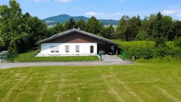 Einfamilienhaus mit großem Garten und Bergblick unter blauem Himmel.