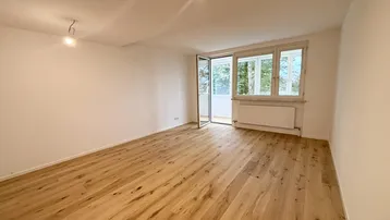 Helles Zimmer mit Holzboden und Zugang zu einem Balkon, ideal als Wohn- oder Schlafzimmer.