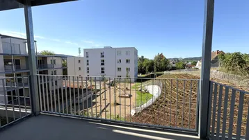 Blick vom Balkon auf die umliegenden Gebäude und eine begrünte Außenanlage unter blauem Himmel.