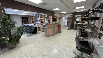 Geräumiger Friseursalon mit Rezeption, mehreren Bedienplätzen und Haarwaschbecken in modernem Design.