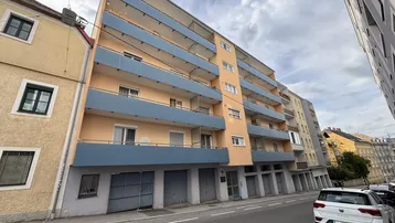 Mehrstöckiges Wohngebäude mit zahlreichen Balkonen und Garagen im Erdgeschoss, an einer Straße gelegen.