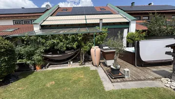 Gepflegter Gartenbereich mit Rasenfläche, Holzterrasse, Hängematte und Whirlpool unter Solarpaneelen.