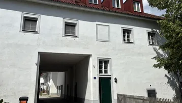 Weiß verputztes Gebäude mit rotem Ziegeldach, Gaubenfenstern und einem Durchgang zum Innenhof.