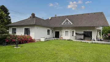Großzügiges Einfamilienhaus mit gepflegtem Rasen und blühenden Büschen unter blauem Himmel.