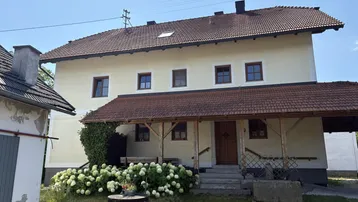 Traditionelles Haus mit überdachtem Eingangsbereich und gepflegter Gartenbepflanzung unter blauem Himmel.