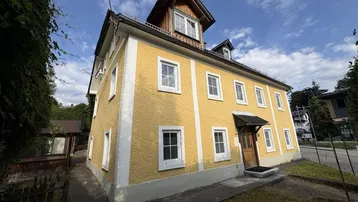 Gelbes Gebäude mit weißen Fenstern und Dachgauben unter blauem Himmel.