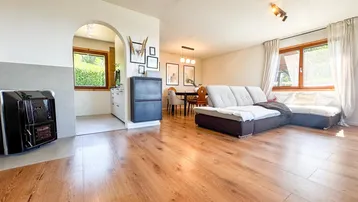 Helles Wohn- und Esszimmer mit Holzboden, gemütlichem Sofa und einem traditionellen Ofen.