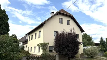 Traditionelles Wohnhaus mit Satteldach und hellgelber Fassade unter bewölktem Himmel.