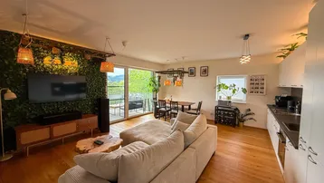 Heller offener Wohn- und Essbereich mit integrierter Küche, Holzboden und Zugang zum Balkon.