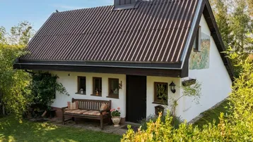 Charmantes kleines Haus mit Satteldach und weißer Fassade, umgeben von grüner Natur.