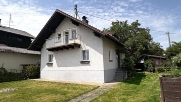 Weiß verputztes Einfamilienhaus mit kleinem Balkon und Vorgarten unter blauem Himmel.
