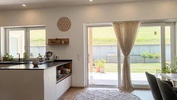 Moderne Küche mit Holzboden, Kücheninsel und großem Schiebefenster zum Garten.