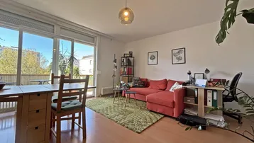 Helles Wohn- und Esszimmer mit Holzboden, gemütlichem Sofa und Zugang zum Balkon.