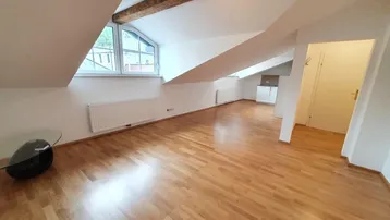 Helles Wohnzimmer im Dachgeschoss mit Holzbalken, Dachschrägen und integrierter Küchenzeile.
