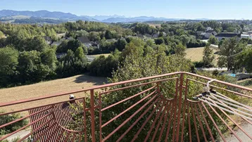 Weitläufiger Ausblick vom Balkon über Felder, Wälder und ferne Berge unter klarem Himmel.
