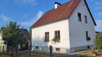Weißes Einfamilienhaus mit rotem Satteldach und kleinem Vorgarten unter blauem Himmel.