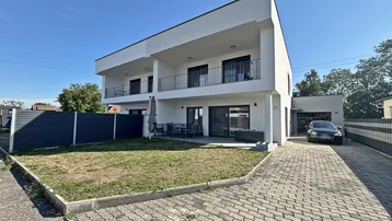 Modernes weißes Gebäude mit Flachdach, Balkonen, Terrasse und gepflasterter Auffahrt.