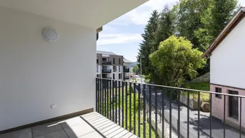 Heller Balkon mit Fliesenboden und modernem Geländer, bietet einen weiten Blick auf die grüne Umgebung und weitere Gebäude.