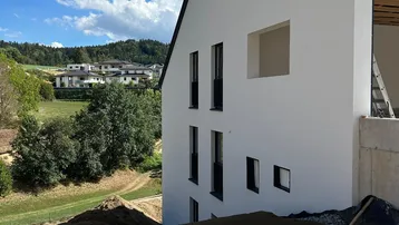 Seitenansicht eines Neubaus mit Blick auf die umliegende Landschaft und weitere Häuser.