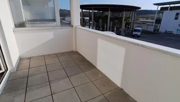 Leerer Balkon mit Fliesenboden und weitem Blick auf die Umgebung unter blauem Himmel.