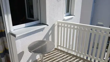 Kleiner sonniger Balkon mit weißem Geländer und einem runden Metalltisch, ideal für eine Kaffeepause.
