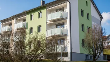 Seitenansicht eines Mehrfamilienhauses mit mehreren Balkonen und moderner Fassadengestaltung.