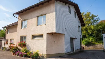Rückansicht des Hauses mit Holzverkleidung und blühenden Topfpflanzen.