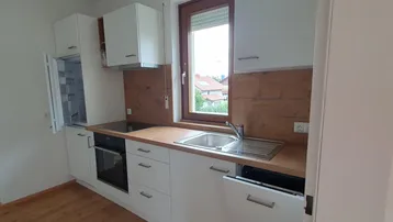 Moderne Einbauküche mit weißen Schränken, Holzarbeitsplatte, integrierten Geräten und Fenster.