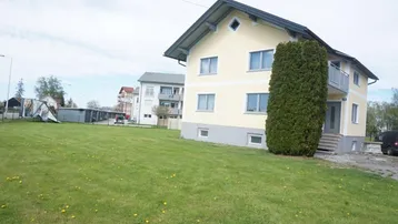 Gelbes Einfamilienhaus mit Satteldach, kleinem Balkon und großem Rasenbereich im Vordergrund.