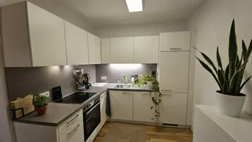 Moderne Einbauküche mit weißen Schränken, grauer Arbeitsplatte und integrierten Geräten.