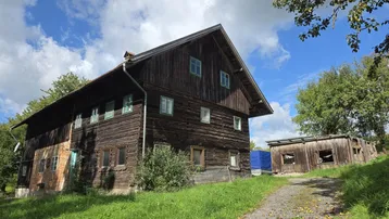 Altes Holzhaus mit traditioneller Bauweise und ländlichem Charme unter blauem Himmel.