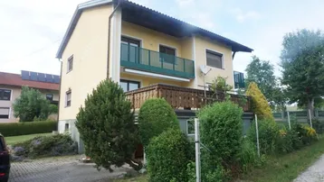 Gelbes Einfamilienhaus mit zwei Balkonen und gepflegtem Vorgarten in ländlicher Umgebung.