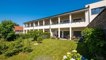 Moderne Wohnanlage mit gepflegtem Garten, Terrassen und Balkonen unter blauem Himmel.