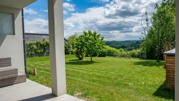 Großer, gepflegter Garten mit Rasenfläche, Baumbestand und einer Terrasse, die einen weiten Blick ins Grüne bietet.