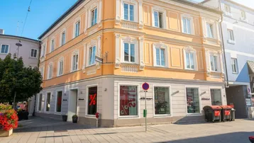 Historisches Gebäude mit orangefarbener Fassade und großen Schaufenstern im Erdgeschoss an einer sonnigen Straße.
