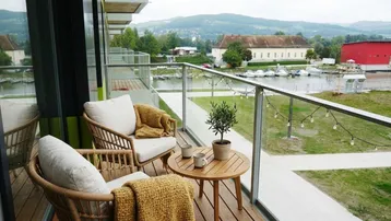 Gemütlicher Balkon mit Holzboden, Sitzgelegenheiten und malerischem Blick auf den See und die Berge.