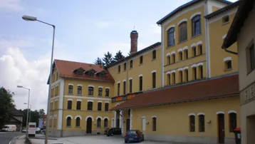 Gelbes Gebäude mit traditioneller Architektur und rotem Ziegeldach, an einer Straße gelegen.