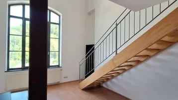 Heller Wohnbereich mit Holztreppe, Laminatboden und großen Fenstern mit Blick ins Grüne.