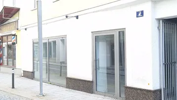 Vorderansicht eines modernen Geschäftsgebäudes mit großen Glasfenstern und Eingangstür zur Straße.