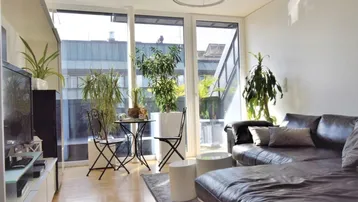 Helles Wohnzimmer mit großem Ledersofa, bodentiefen Fenstern und vielen Pflanzen.