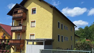 Gelbes Mehrfamilienhaus mit traditionellen Holzbalkonen unter blauem Himmel.