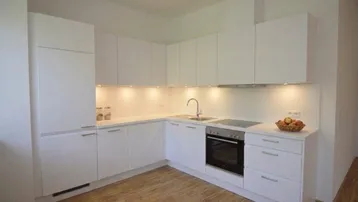 Moderne weiße Einbauküche mit Holzfußboden und integrierten Geräten in hellem Raum.